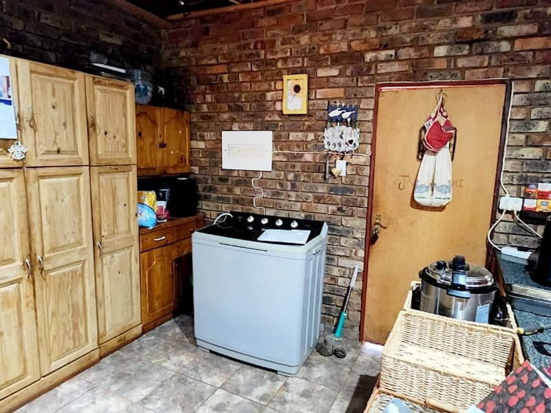 A functional laundry area featuring exposed brick walls, tiled flooring, and built-in wooden cabinetry providing ample storage space.