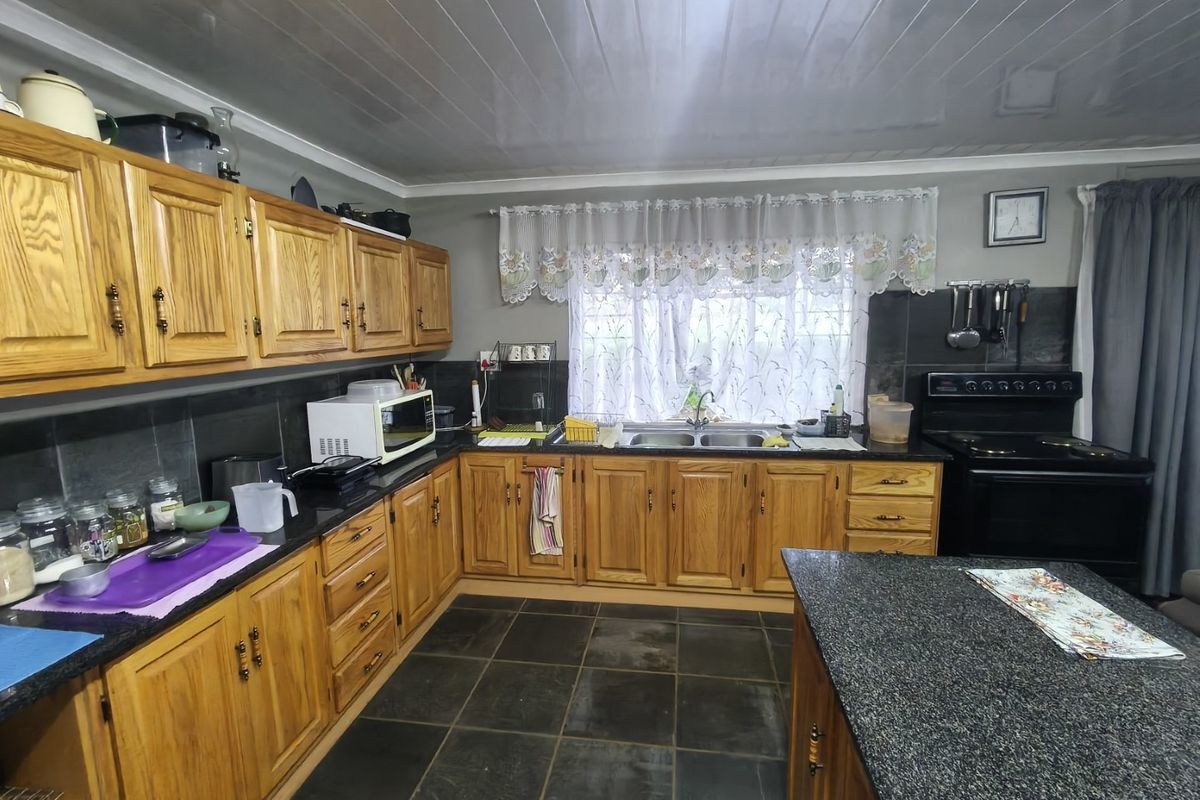 A functional kitchen featuring wooden cabinetry, granite countertops, a double basin sink, and a central island, with dark tiled flooring throughout.