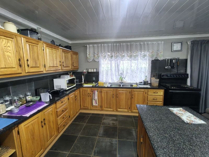A functional kitchen featuring wooden cabinetry, granite countertops, a double basin sink, and a central island, with dark tiled flooring throughout.