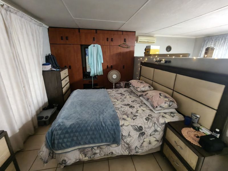 A bedroom featuring built-in wooden cupboards, tiled flooring, and a wall-mounted split-system air conditioning unit.