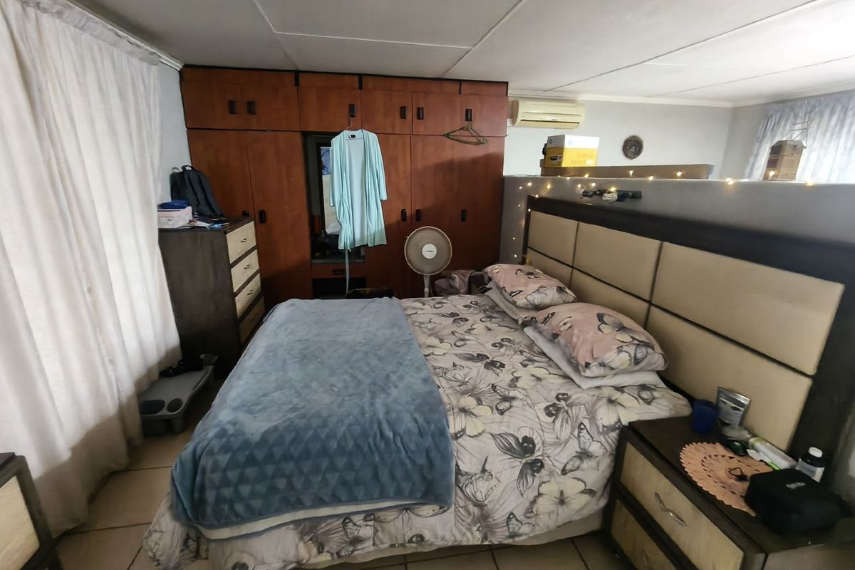 A bedroom featuring built-in wooden cupboards, tiled flooring, and a wall-mounted split-system air conditioning unit.