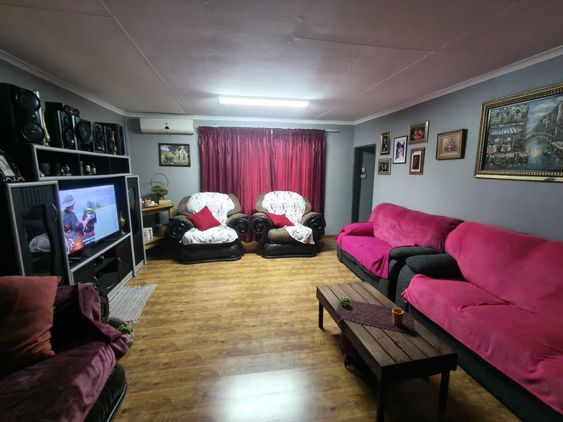A spacious living room featuring laminate flooring, a wall-mounted air conditioning unit, and coved ceiling detailing.