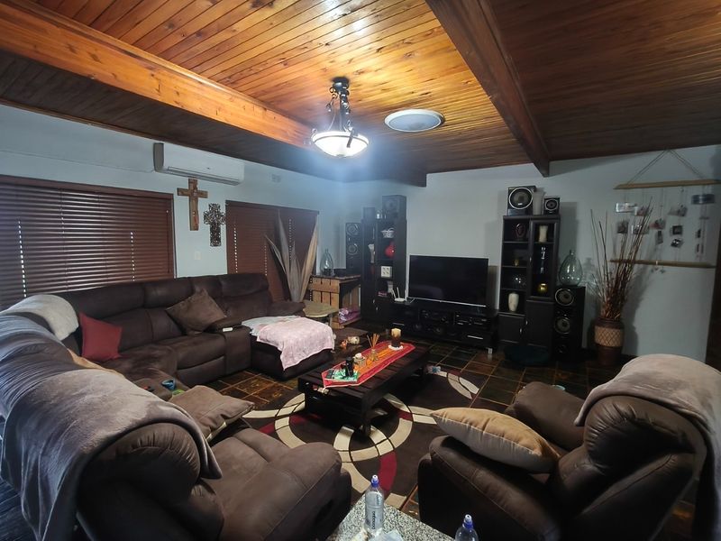 A cozy living room featuring a distinctive timber-clad vaulted ceiling with exposed beams, tiled flooring, and a wall-mounted split-system air conditioner.