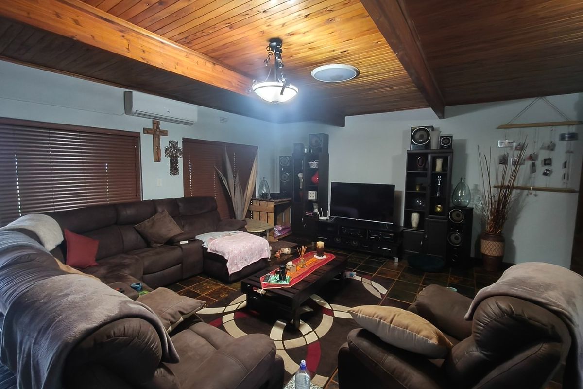 A cozy living room featuring a distinctive timber-clad vaulted ceiling with exposed beams, tiled flooring, and a wall-mounted split-system air conditioner.