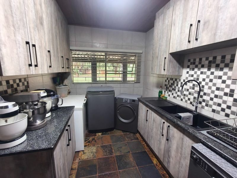 A functional scullery featuring modern wood-look cabinetry, granite countertops, a double basin sink, and durable slate flooring with integrated laundry appliance connections.