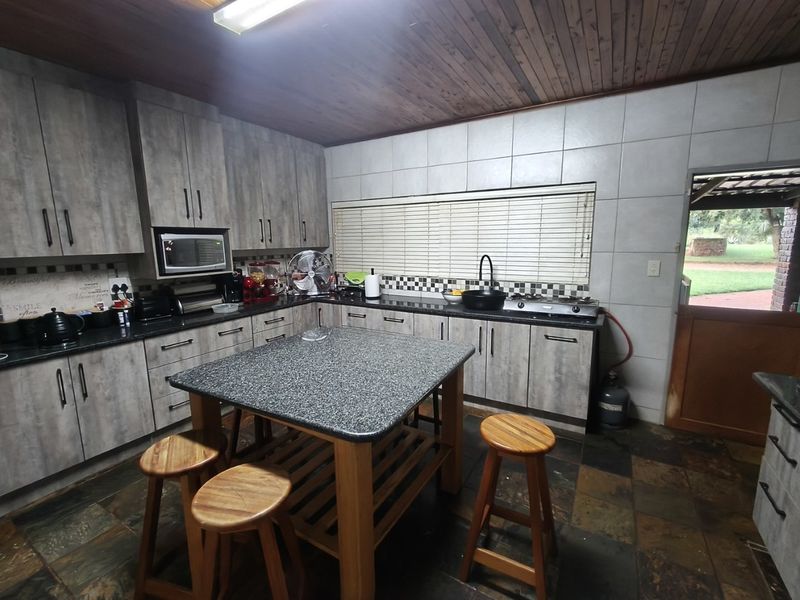 A functional kitchen featuring grey wood-look cabinetry, granite countertops, a gas hob, and slate tile flooring with a timber-clad ceiling.