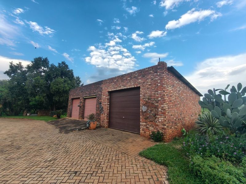 A detached brick garage building featuring three roller shutter doors and a paved driveway, situated on a farm property.