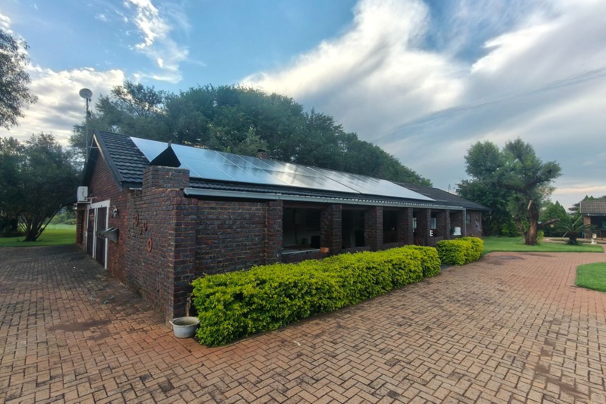 A rear view of a brick farm building featuring a large solar panel array on the roof and an expansive paved driveway area.
