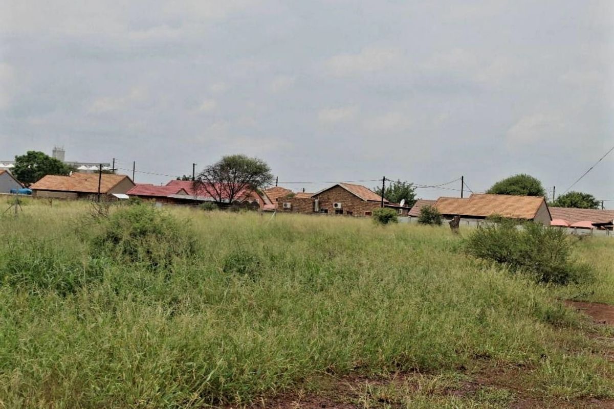 A view of a vacant residential plot featuring natural grassland with surrounding neighborhood houses in the background.