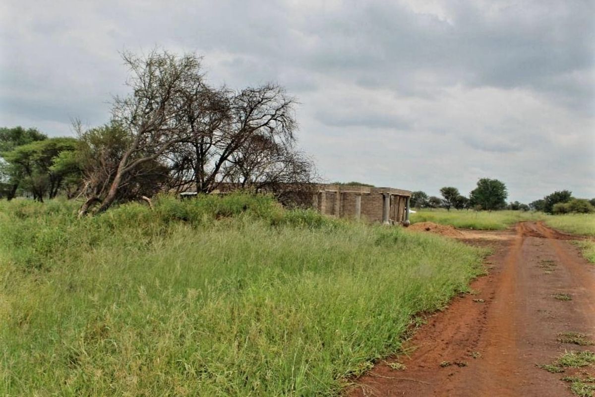 A view of a vacant residential plot featuring a partially constructed building shell and an unpaved access road.