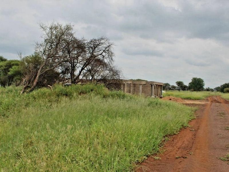A view of a vacant residential plot featuring a partially constructed building shell and an unpaved access road.