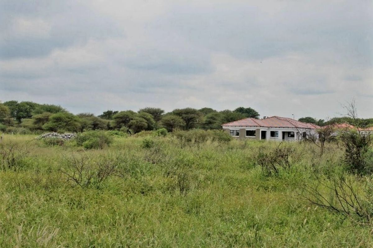 A view of a residential plot featuring an unfinished building structure surrounded by overgrown natural vegetation.