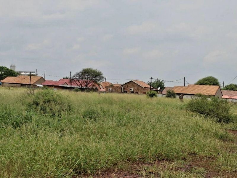 A view of a vacant residential plot featuring natural grassland with surrounding neighborhood houses in the background.
