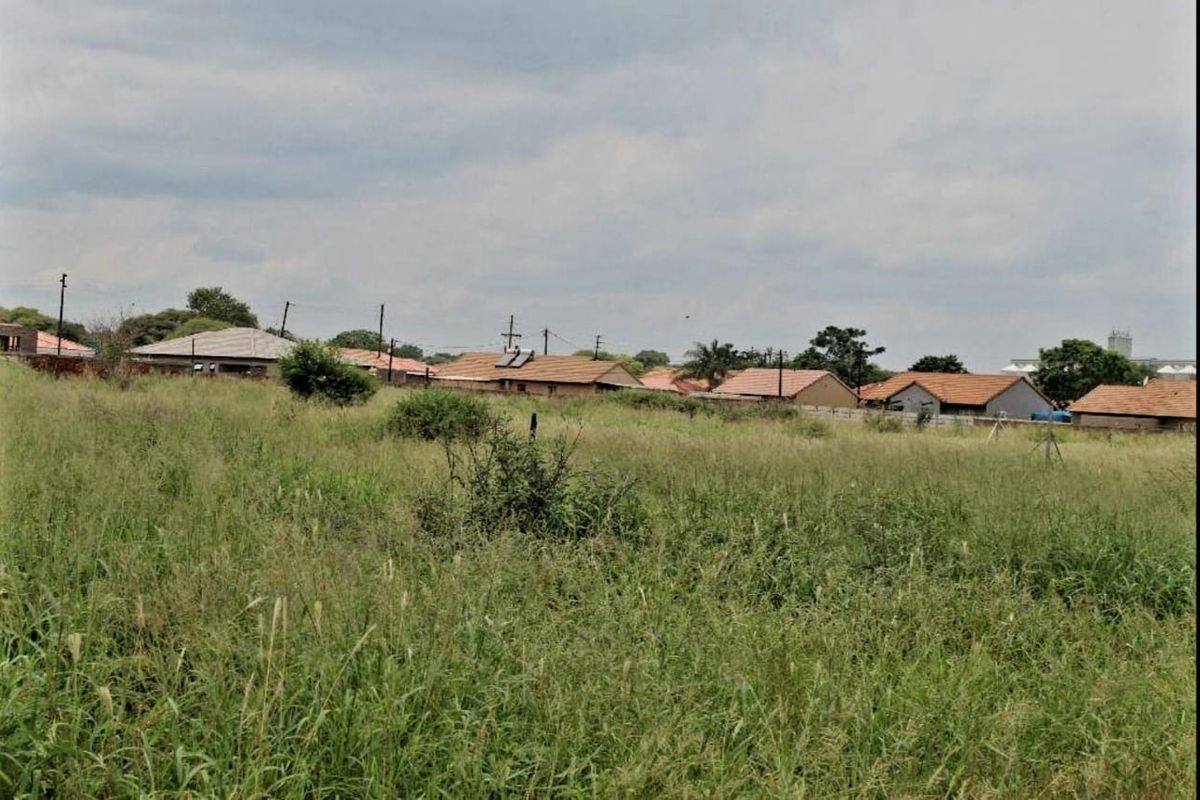 A view of an undeveloped residential plot of land with surrounding neighborhood houses visible in the background.