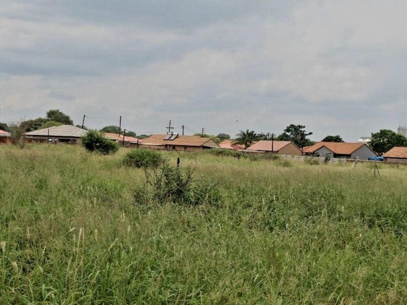 A view of an undeveloped residential plot of land with surrounding neighborhood houses visible in the background.
