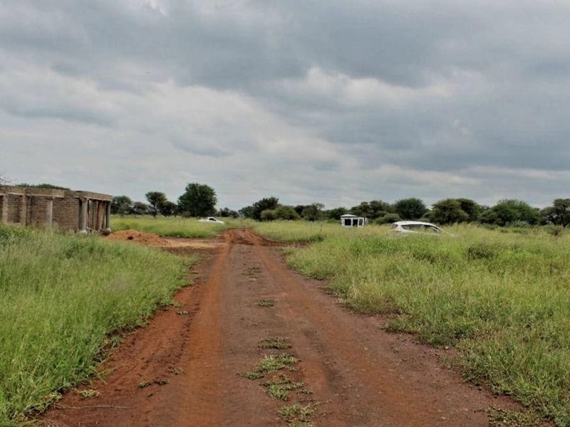 A view of a vacant residential plot featuring a dirt access road and an unfinished building structure on the property.