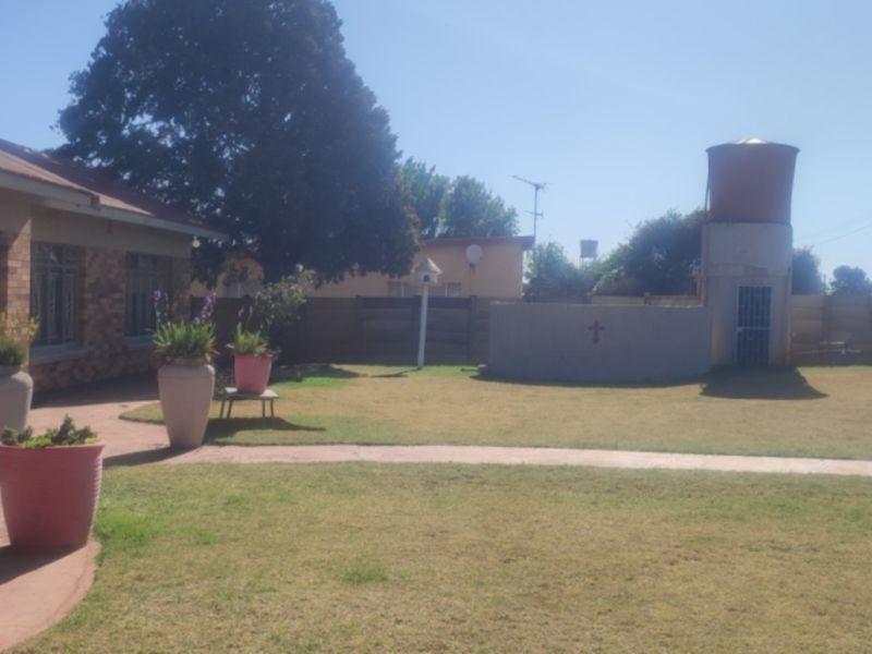 Rear view of the property featuring a brick facade, a paved walkway, and a water tank situated in the garden area.