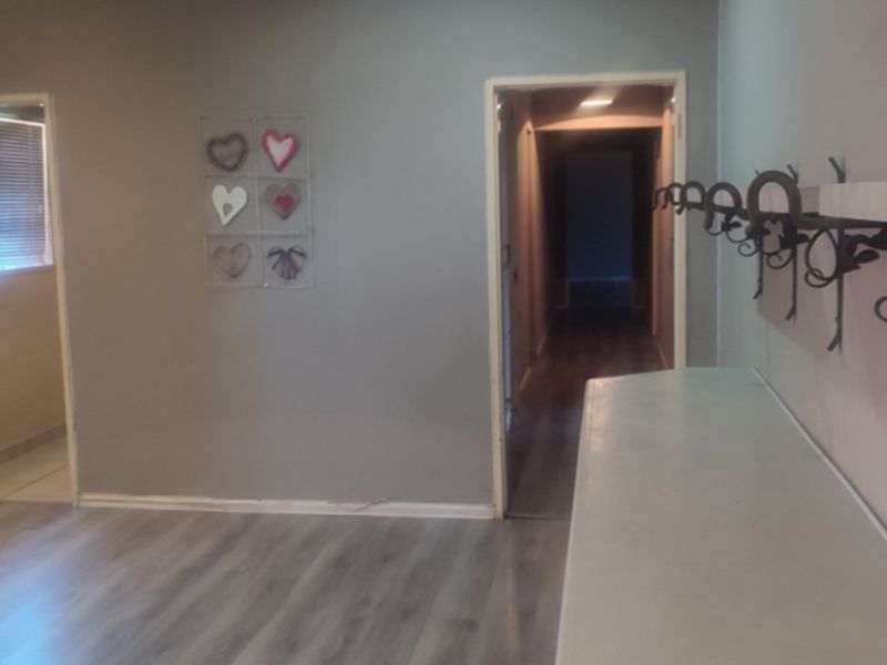 A spacious hallway featuring modern laminate flooring, built-in shelving, and decorative wrought iron wall hooks, providing a functional transition space between rooms.