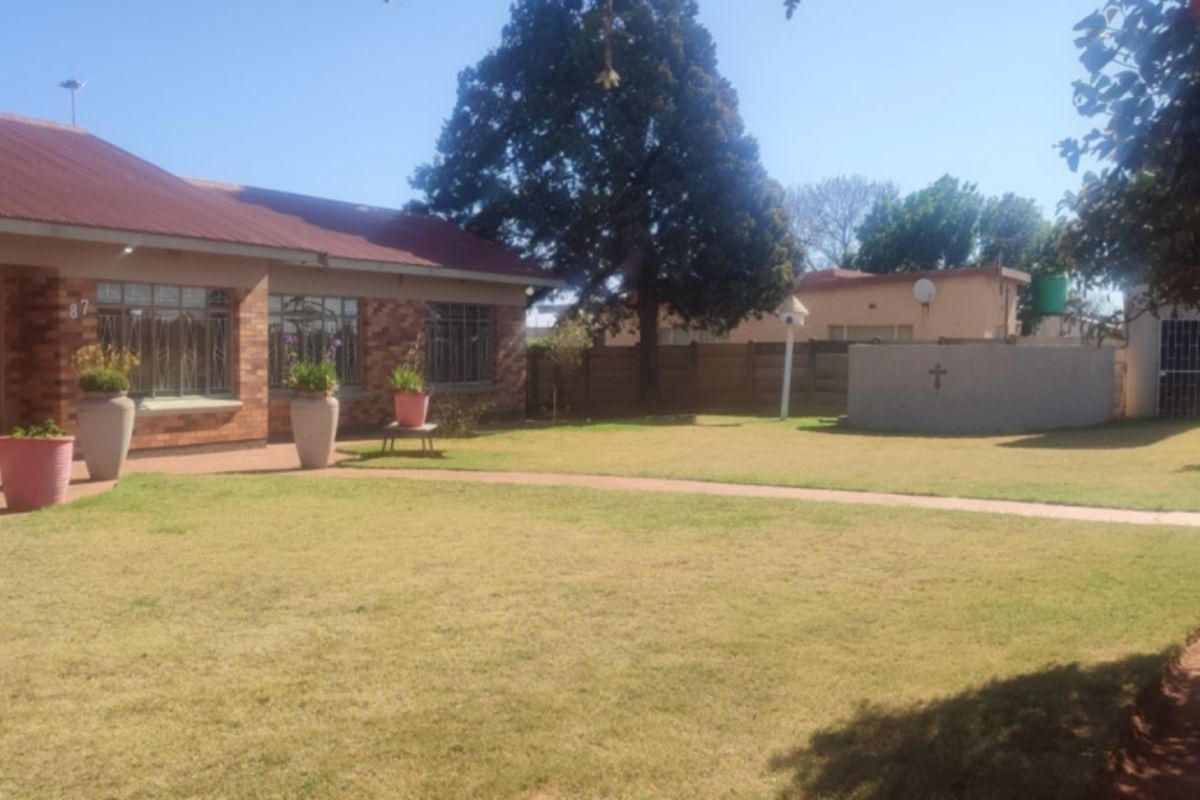 A view of the rear garden featuring a brick house facade, a well-maintained lawn, and a concrete boundary wall.