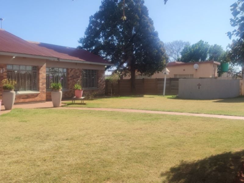 A view of the rear garden featuring a brick house facade, a well-maintained lawn, and a concrete boundary wall.