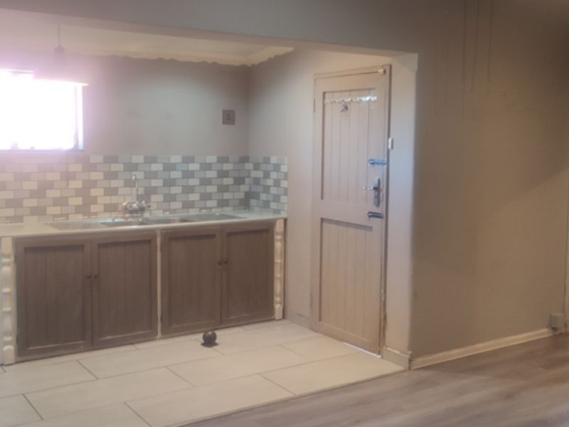 A functional kitchen area featuring built-in cabinetry, a tiled backsplash, and a sink, with neutral wall tones and a mix of tiled and laminate flooring.