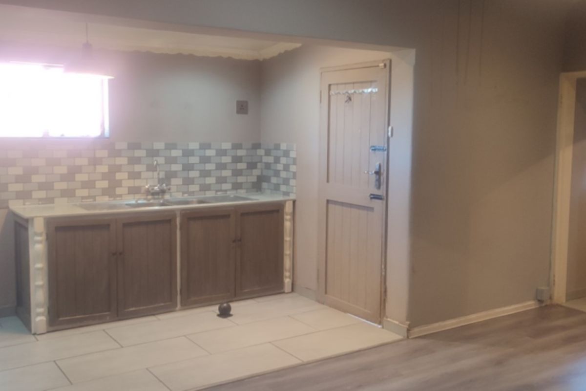 A functional kitchen area featuring built-in cabinetry, a tiled backsplash, and a sink, with neutral wall tones and a mix of tiled and laminate flooring.