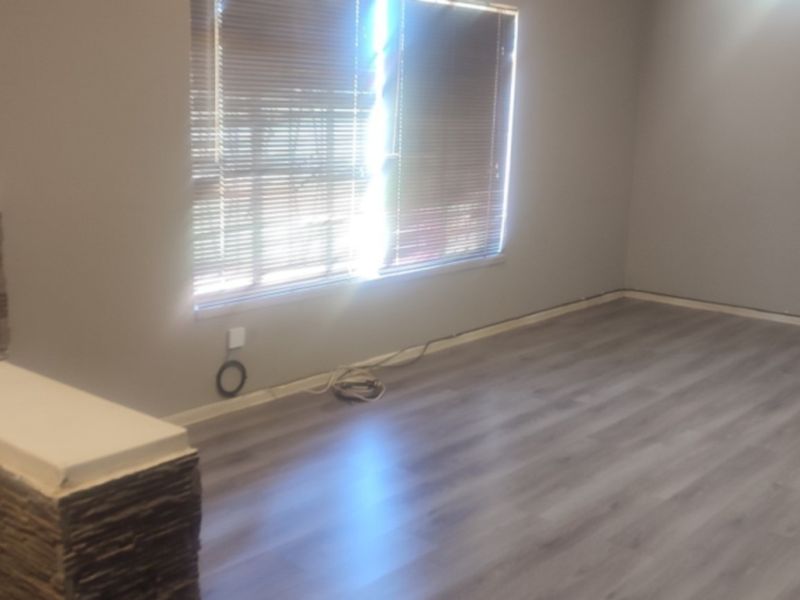 An empty living room featuring modern grey laminate flooring, a decorative stone-clad pillar, and venetian blinds, currently awaiting final finishing touches.