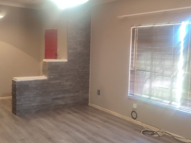 A spacious living area featuring modern laminate flooring, a decorative stone-cladding feature wall, and large windows fitted with venetian blinds.