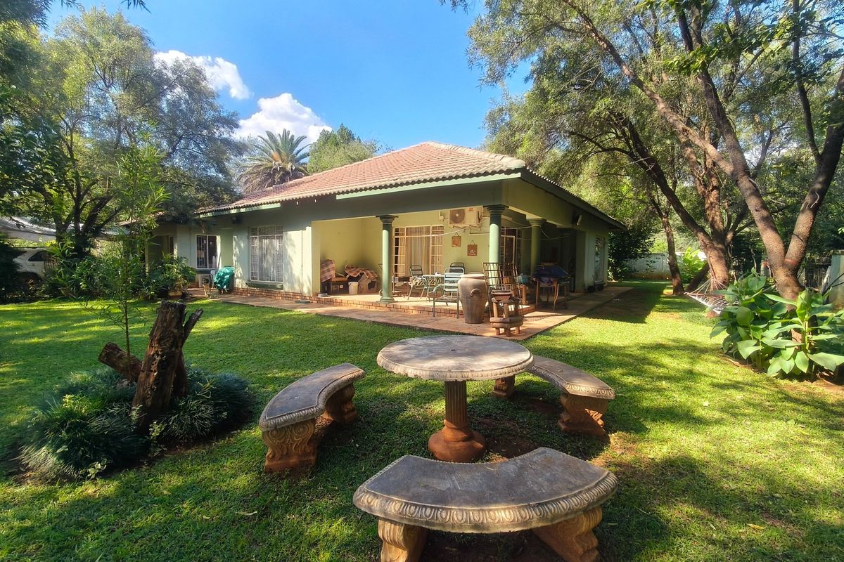 Rear view of the farmhouse featuring a spacious covered patio, tiled roof, and established garden surroundings.