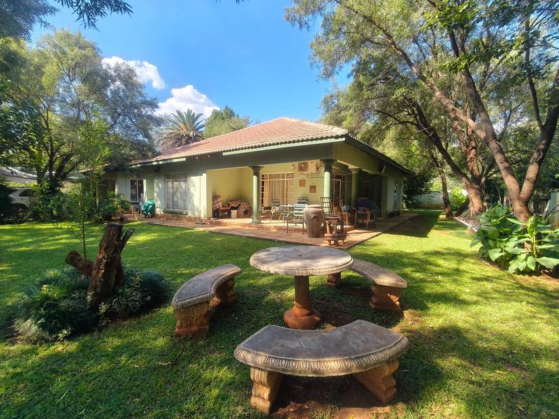 Rear view of the farmhouse featuring a spacious covered patio, tiled roof, and established garden surroundings.