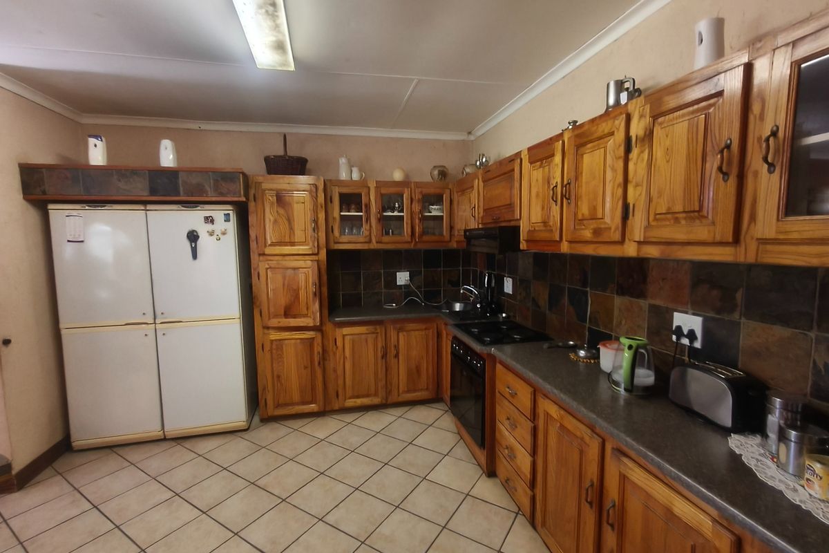 A functional kitchen featuring traditional wooden cabinetry, stone tile backsplash, built-in oven, and electric hob with ample counter space and tiled flooring.