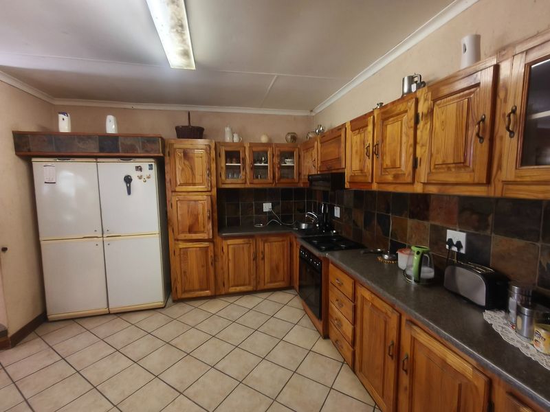 A functional kitchen featuring traditional wooden cabinetry, stone tile backsplash, built-in oven, and electric hob with ample counter space and tiled flooring.
