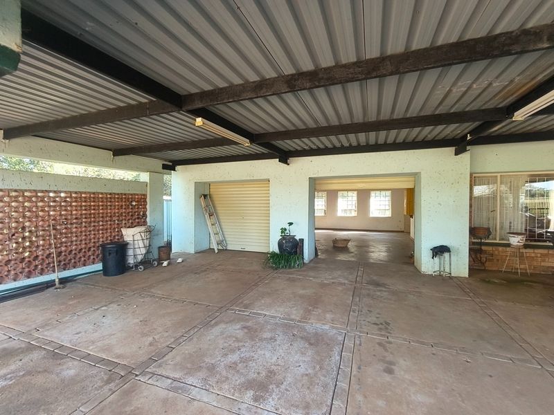 A spacious covered patio area featuring a decorative brick screen wall, concrete flooring, and direct access to the main dwelling through a roll-up door.