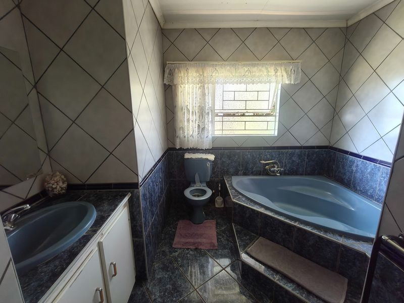 A dated bathroom featuring a corner bathtub, built-in vanity with basin, and toilet, finished with dark blue tiled surfaces and diamond-patterned wall tiles.