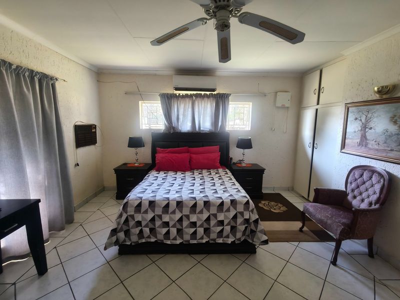 A functional bedroom featuring tiled flooring, built-in cupboards, a ceiling fan, and a wall-mounted air conditioning unit.