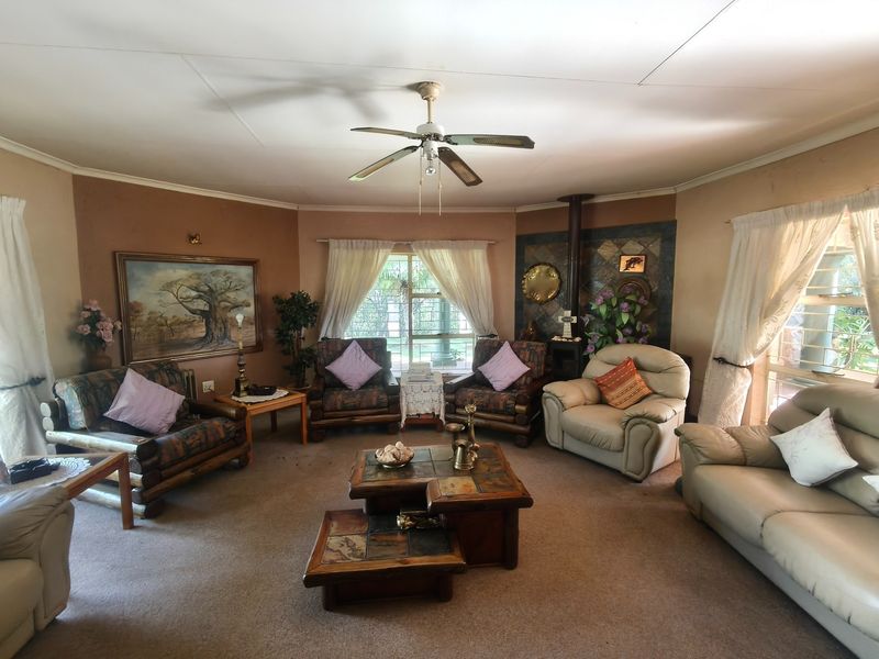 Spacious living room featuring a wood-burning stove with tiled surround, ceiling fan, and large windows with security bars.