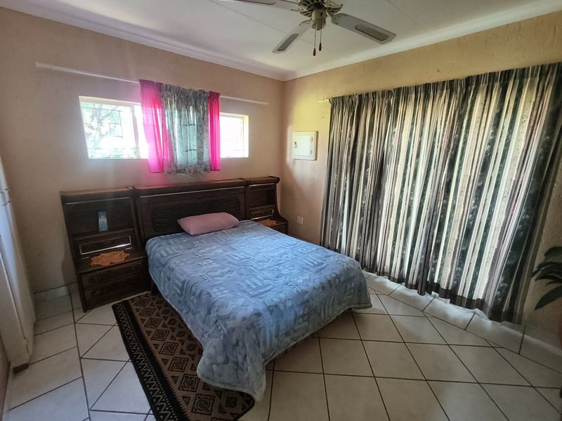 A bedroom featuring tiled flooring, a ceiling fan, and a built-in headboard, with access to the outdoors via a sliding glass door.
