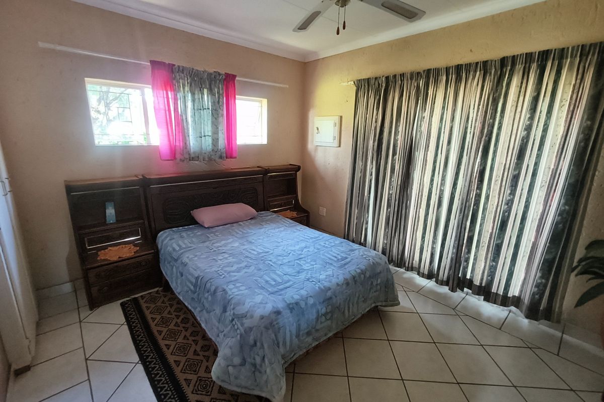 A bedroom featuring tiled flooring, a ceiling fan, and a built-in headboard, with access to the outdoors via a sliding glass door.
