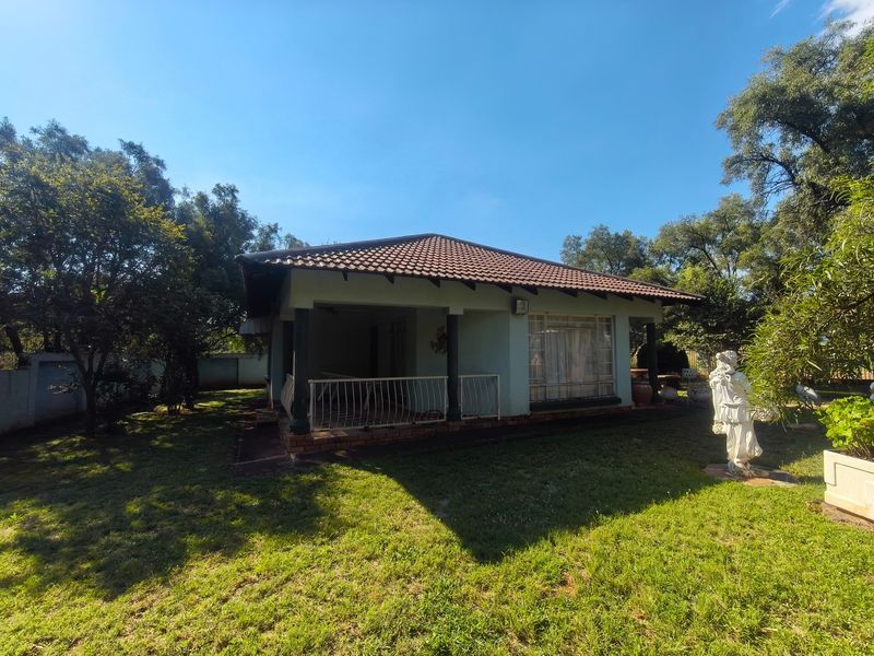 A view of the rear elevation of the farm house featuring a covered patio, tiled roof, and established garden surroundings.