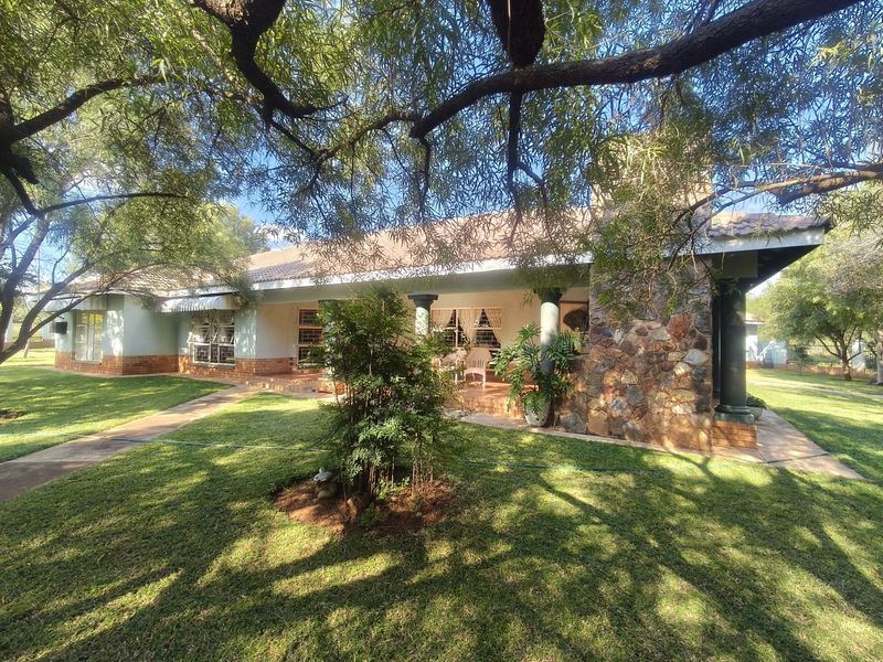 A charming farm-style home featuring stone cladding, a covered patio, and a well-maintained garden under mature trees.