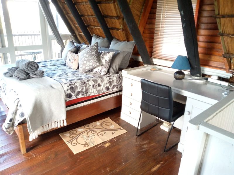 A rustic bedroom featuring exposed timber rafters, a thatched roof ceiling, and timber flooring, with a built-in desk area.