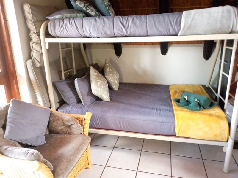 A bedroom featuring tiled flooring and a traditional thatched ceiling, currently furnished with a bunk bed.