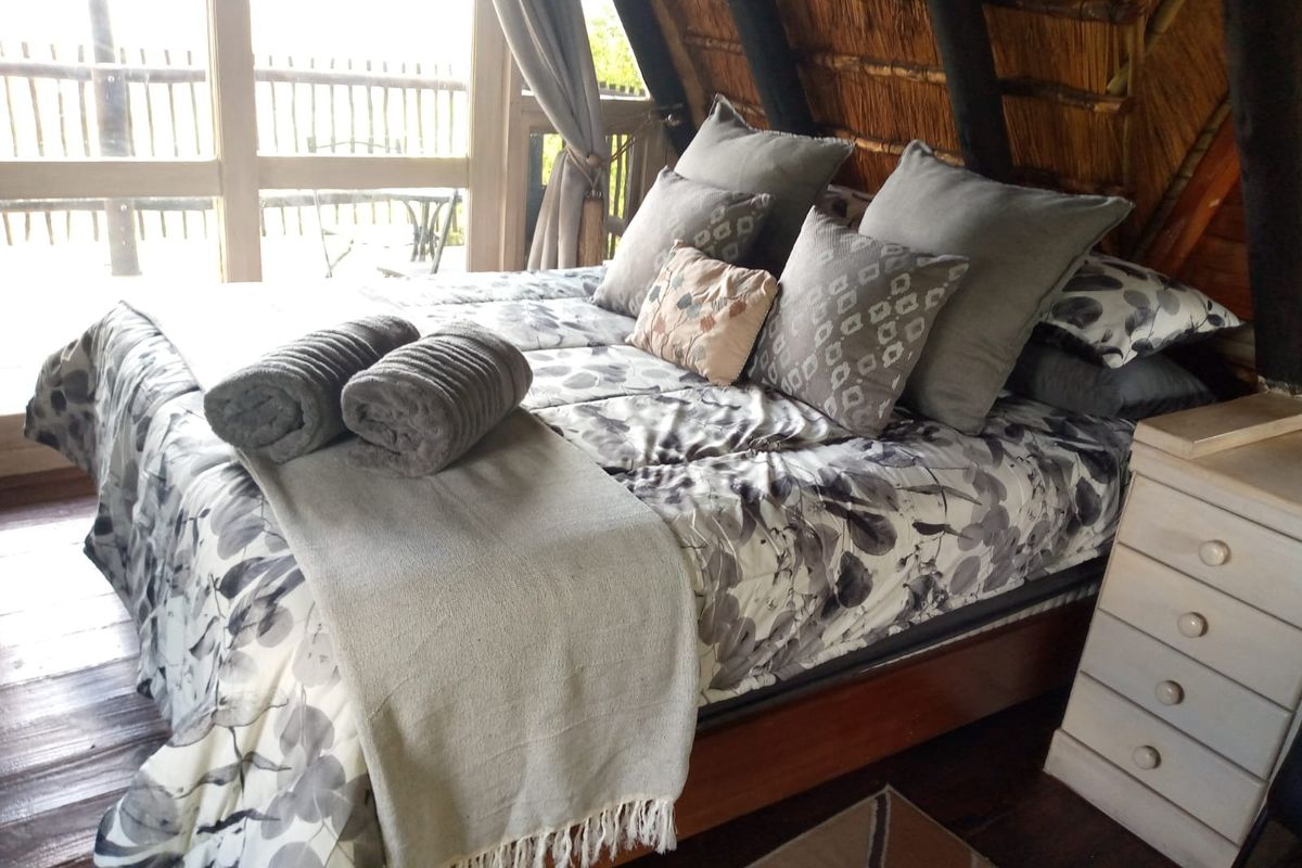 A cozy bedroom featuring a unique thatched roof design, timber flooring, and large glass doors that provide natural light and access to the outdoors.