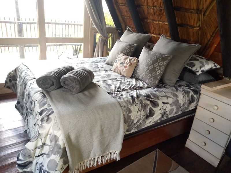 A cozy bedroom featuring a unique thatched roof design, timber flooring, and large glass doors that provide natural light and access to the outdoors.