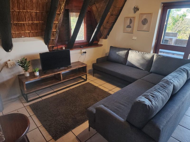 Cozy living room featuring a unique thatched roof with exposed timber rafters and tiled flooring, providing a rustic and warm atmosphere.