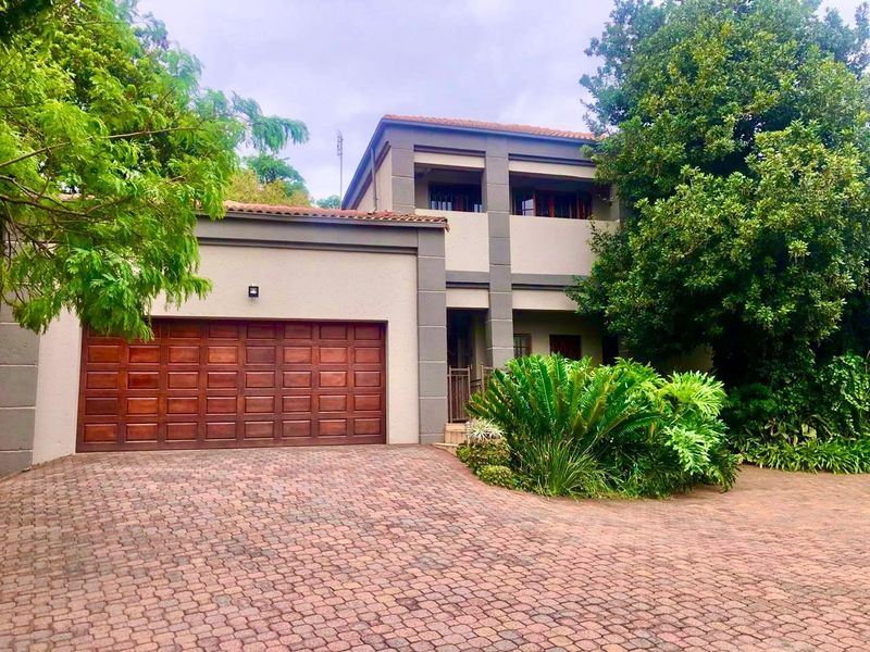 Front elevation of a two-story residential property featuring a wooden double garage door, paved driveway, and established garden landscaping.