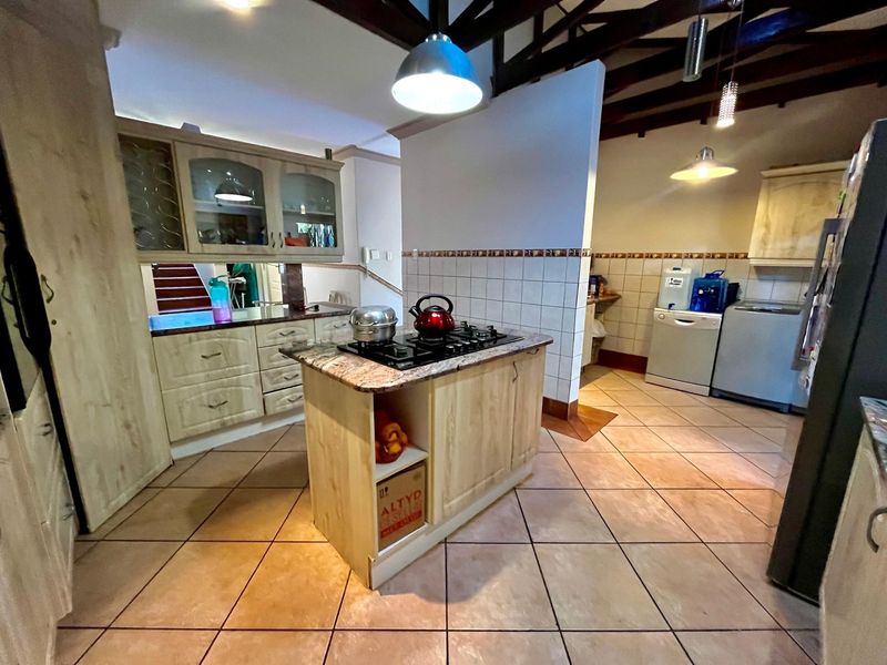 Spacious kitchen featuring a central island with a gas hob, granite countertops, ample cabinetry, and exposed timber beams under a high ceiling.