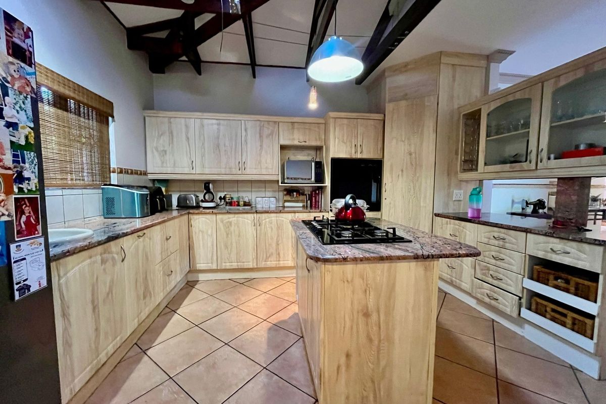Spacious kitchen featuring light wood cabinetry, granite countertops, a central island with a gas hob, and exposed timber beams under a vaulted ceiling.