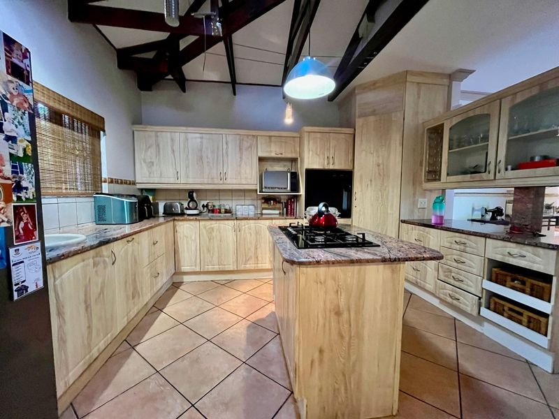 Spacious kitchen featuring light wood cabinetry, granite countertops, a central island with a gas hob, and exposed timber beams under a vaulted ceiling.