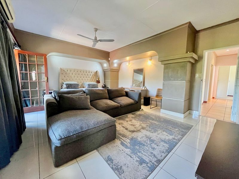 Spacious bedroom featuring tiled flooring, a ceiling fan, wall-mounted air conditioning, and a unique built-in architectural alcove for the bed area.